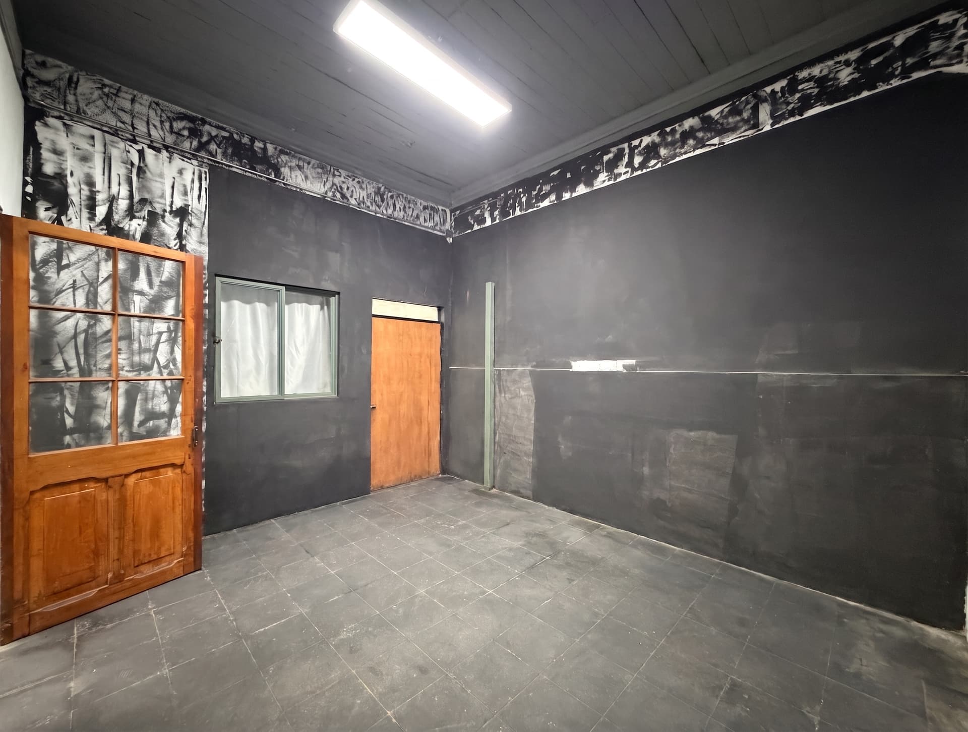 Espacio 4 en la sede Salvador, Ñuñoa — Sala de carácter industrial, con muros oscuros, piso de baldosa y puerta de madera. Pensada para producir e instalar equipos.